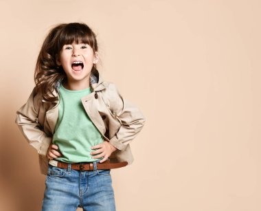 Joyful dark-haired baby in a beige coat, happy smiles on a beige background