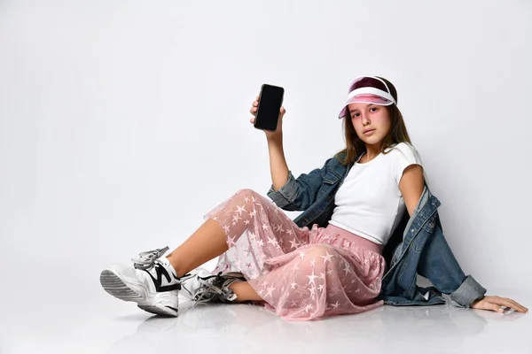 一个快乐的女人坐在地板上，用浅色的背景显示一个空白的智能手机屏幕 — 图库照片