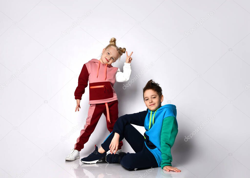 Children, brother and sister, in colorful tracksuits and sneakers. They looking at each other, smiling, posing isolated on white