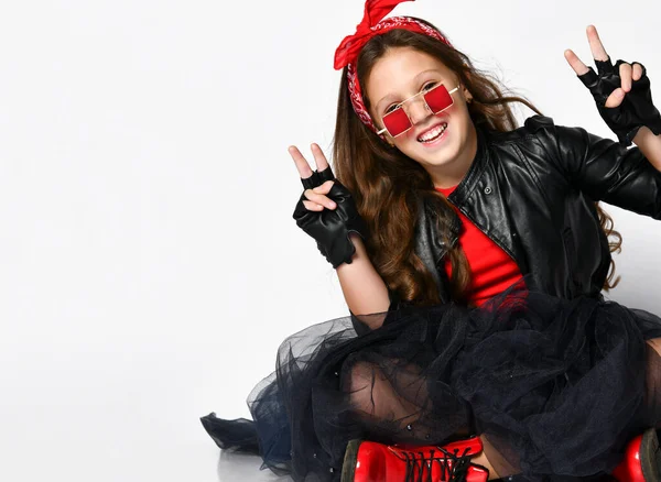 Joven modelo de chica positiva en estilo rock brillante ropa casual y botas rojas sentadas en el suelo y mostrando signo de paz con los dedos — Foto de Stock
