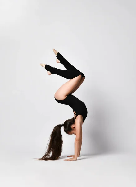 Gimnasta adolescente en maillot negro, calcetines de rodilla y zapatillas de ballet, realizando ejercicios de pie sobre sus manos, boca abajo, aislada en blanco. Primer plano — Foto de Stock