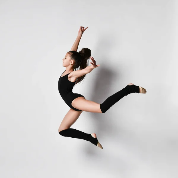 Ginnasta adolescente bruna con codino, in body nero, calze al ginocchio e scarpe da ballo, che esegue esercizi, posa isolata sul bianco. Primo piano . — Foto Stock