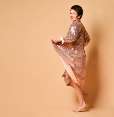 Kısa saçlı, gülümseyen esmer bir kadın seksi, parlak bir gece kostümü ve çıplak ayaklı bir elbisesi var.