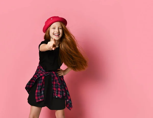 Roodharig tienerkind in zwarte jurk, geruit hemd aan de taille, rode hoed. Wijzend naar jou, poserend op een roze achtergrond. Sluiten. — Stockfoto