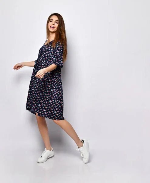 Modelo morena en vestido negro con estampado floral, zapatillas blancas. Sonriendo, tocándose la cara, posando aislada sobre blanco. Longitud completa —  Fotos de Stock