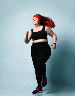 Mavi arka planda koşan mutlu, kızıl saçlı, tombul bayan. Fitness, fiziksel aktivite, vücut pozitifliği. Tam boy portre, kopyalama alanı