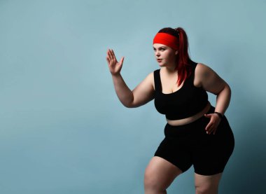 Ciddi bir şekilde konsantre olmuş, iri yarı genç bayan, kolları mavi arka planda bükülmüş, bacakları bükülmüş ve kolları bükülmüş olarak yukarı bakarak egzersiz yapıyor. Fitness. Boşluğu kopyala