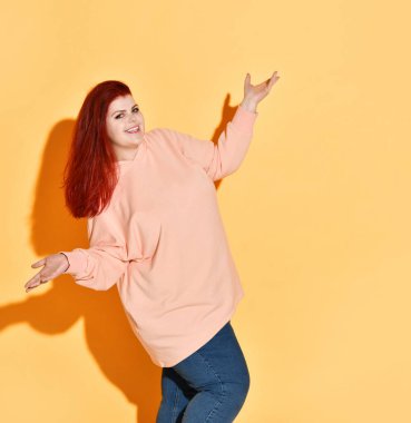 Heyecanlı gülümseyen tombul bayan başarısından dolayı mutlu. Avuçlarını açık tutarak el hareketi yapıyor. Stüdyo çekimi turuncu üzerine izole edildi