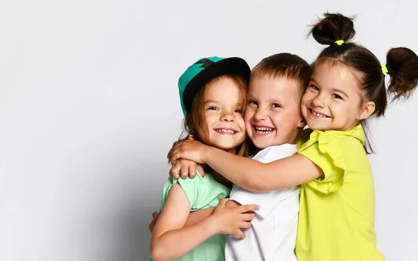 Retrato de estudio de niños sobre un fondo claro: toma de cuerpo completo de tres niños con ropa brillante, dos niñas y un niño. Trillizos, hermanos y hermanas. abrazo en cámara. Lazos familiares, amistad — Foto de Stock