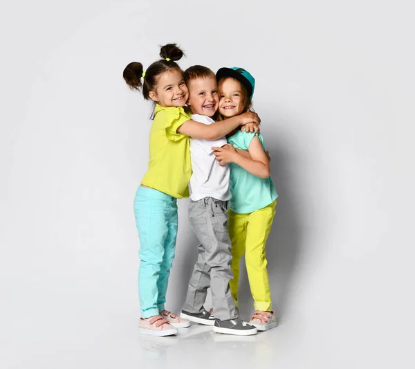 Stúdió portré a gyermekek egy könnyű háttér: teljes test lövés három gyermek fényes ruhában, két lány és egy fiú. — Stock Fotó