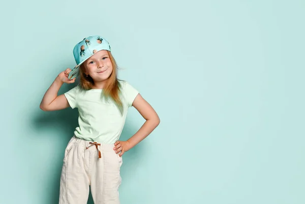 穿着T恤，白裤子的小女人。她笑着，用菠萝印在帽子上，在蓝绿色的背景下摆姿势。靠近点 — 图库照片