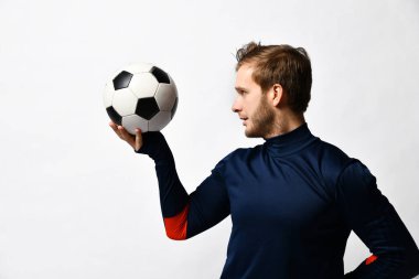 Sarışın adam, mavi eşofmanlı profesyonel futbolcu bir top atacak, beyaz üzerine yanlamasına poz verecek. Kapat.