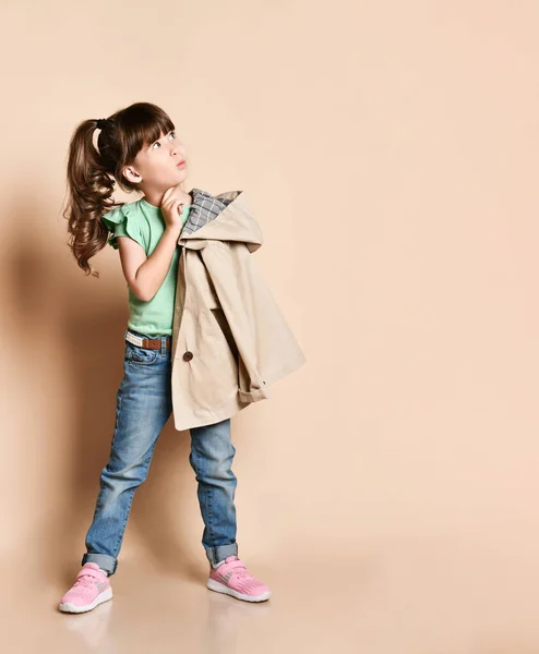Schattig meisje poseren in verschillende poses, in jeans met riem, groen t-shirt en beige jas en roze sneakers — Stockfoto