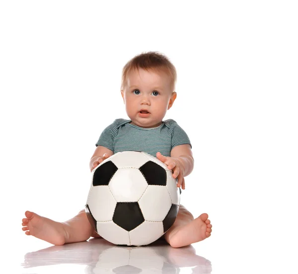 Baby pojke sitter och spelar en klassisk fotboll på en vit bakgrund. Stockfoto