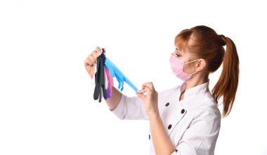 Laboratuvar önlüklü ve tek kullanımlık maskeli kadın doktor ellerinde farklı lateks eldiven örnekleri üzerinde çalışıyordu. Belden yukarı atış, beyaza izole edilmiş.