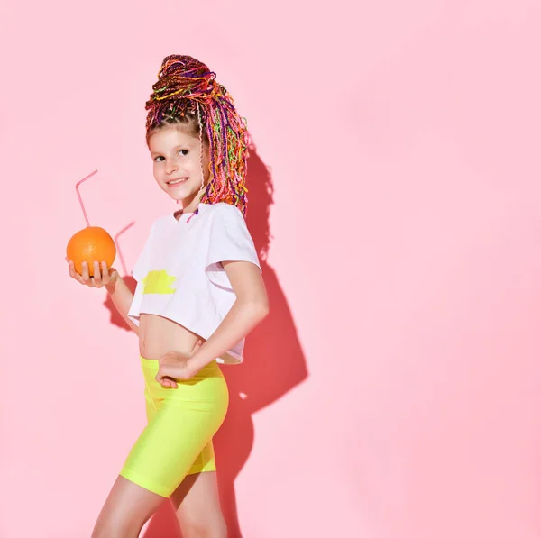 Niña con rastas de colores sosteniendo una naranja con un tubo de cóctel. — Foto de Stock