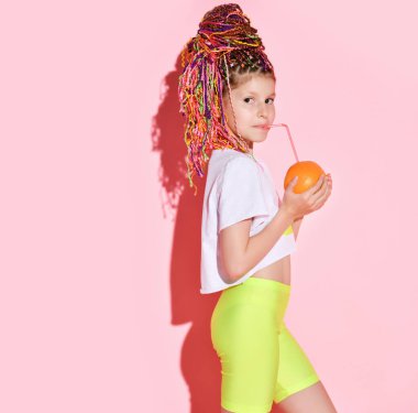 Afrikalı at kuyruklu genç kız elinde turuncuyla tüple içiyor ve pembe arka planda yan pozlar veriyor. Kapat.