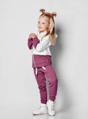 Spor kıyafetlerle poz veren mutlu küçük kız ve gri arka planda spor ayakkabılar..