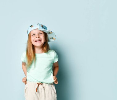 Mavi yaz elbisesi ve ananas desenli şık şapkalı neşeli küçük kız el ele tutuşarak kahkahalar atıyor. Mavi üzerine izole edilmiş, kopyalama alanı