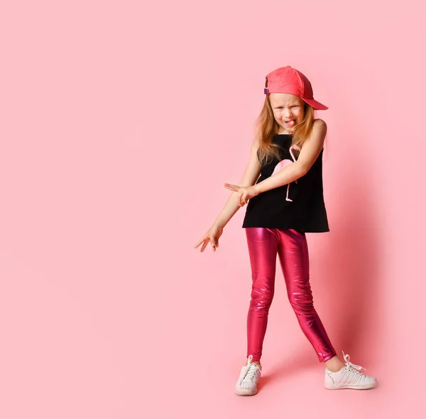 滑稽的小女孩穿着时髦的夏装，戴着帽子，面带微笑，在看相机的时候还在闲聊。全长镜头，粉红色隔离，复制空间 — 图库照片