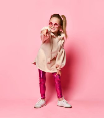 Gülümseyen küçük kız anaokulu öğrencisi midillisi seni işaret etmek için sabırsızlanıyor. Yakın çekim, pembe üzerinde izole edilmiş, kopyalama alanı