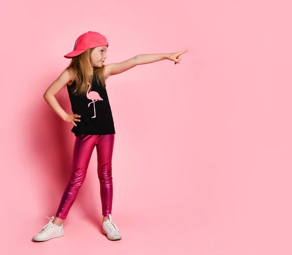 Menina bonito sobre a parede rosa aponta com confiança o dedo para o lado. — Fotografia de Stock