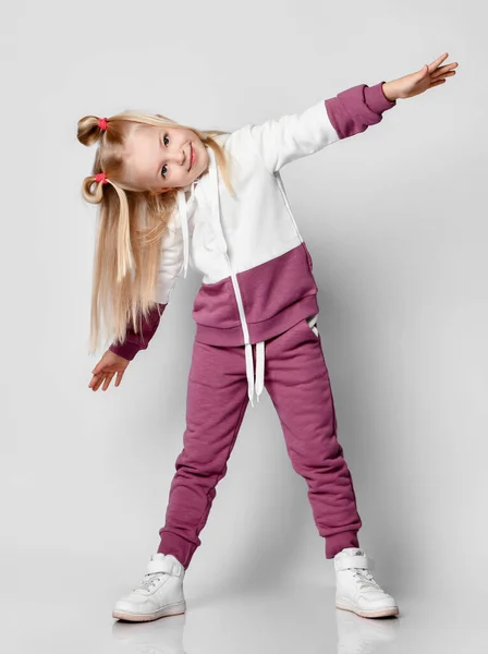 Klein meisje in sportkleding plezier hebben in de studio op een grijze achtergrond. — Stockfoto