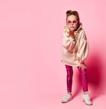 Pembe elbiseli, yuvarlak gözlüklü, ciddi bir kız. Seyirciye öpücük yolluyor. Tam uzunlukta çekim pembe üzerinde izole edildi, kopyala boşluk