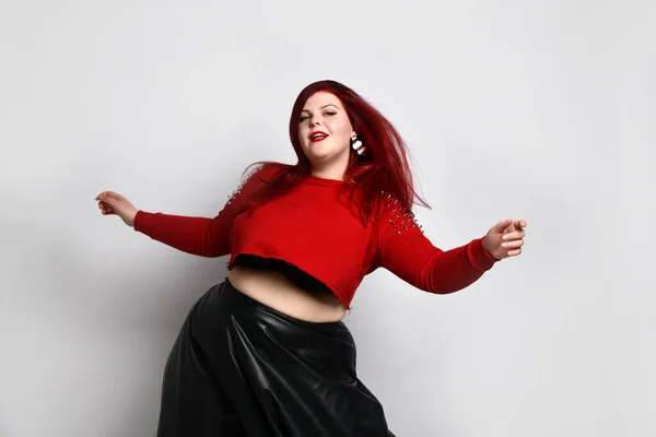 Obese gember dame in rode spiked top, zwarte beha en lederen rok. Ze danst, poseert geïsoleerd op witte foto achtergrond — Stockfoto
