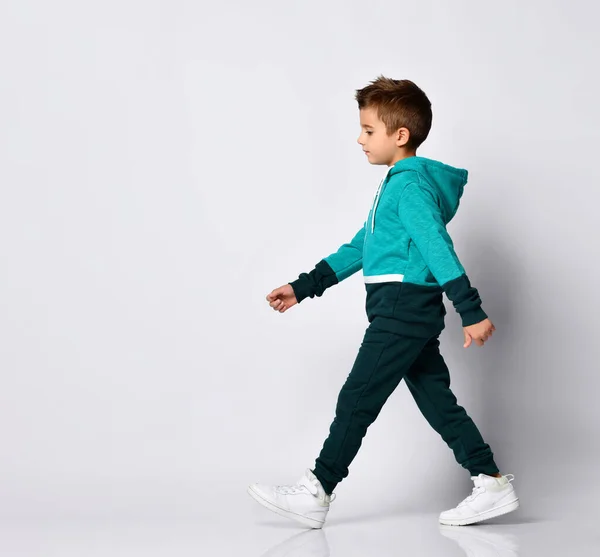 Kleine brünette Junge in einem Sportanzug posiert auf einem grauen Hintergrund. — Stockfoto