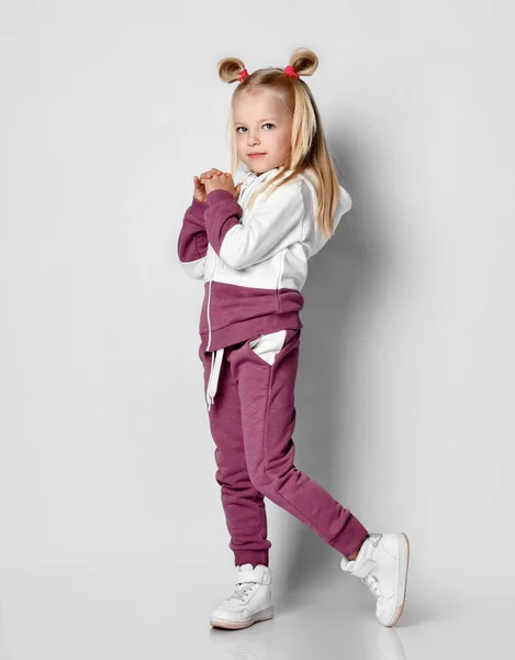 Klein gelukkig lachend meisje poseren in sportkleding en sneakers op grijze achtergrond. — Stockfoto
