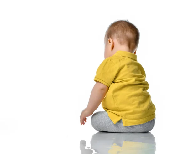 Petit bébé dans un polo jaune assis à côté de nous sur le sol, tournant la tête, regardant un fond blanc. — Photo