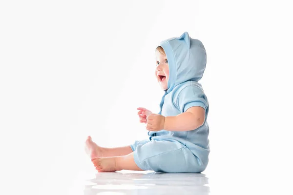 Baby in funny blue suit sit on floor showing tongue — Stock Photo, Image