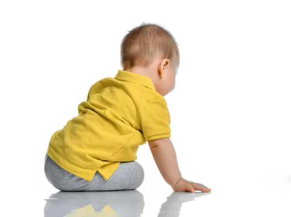 노란 폴로를 탄 작은 아기가 우리 옆 바닥에 앉아 고개를 돌려 하얀 배경을 바라봅니다. — 스톡 사진