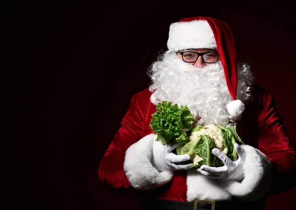 Jolly Santa Claus holds in one hand a bunch of lettuce in another swing of cauliflower. The choice. Enjoy a healthy Christmas dinner. Healthy Christmas Recipes. — Stock Image Jolly Santa Claus holds in one hand a bunch of lettuce in another swing of cauliflower. The choice. Enjoy a healthy Christmas dinner. Healthy Christmas Recipes. Royalty Free Stock Photos