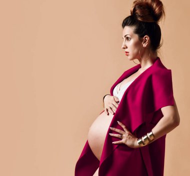 Küpeli esmer anne, bilezik, beyaz iç çamaşırı ve kırmızı şal. Sandalyeye yan oturup, bej arka planda poz vermek. Yakın plan.