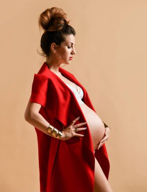 Küpeli esmer anne, bilezik, beyaz iç çamaşırı ve kırmızı şal. Sandalyeye yan oturup, bej arka planda poz vermek. Yakın plan.