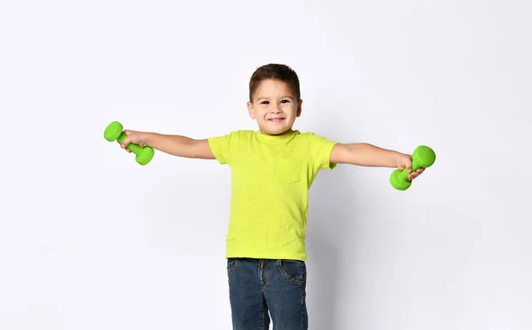Little boy in yellow t-shirt, denim shorts, khaki sneakers. Smiling, holding green dumbbells behind back, posing isolated on white — Stock Photo, Image