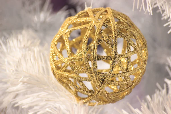 Braided shiny gold ball hangs on a white spruce. Decorations for the Christmas tree. Iridescent light in the reflection of the ball. new year mood. screensaver, background for postcards