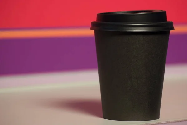 black paper Cup with plastic lid. coffee or takeaway on violet and pink background. brutal glass