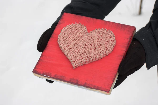 panels of thread and nails, heart on a red background. string art on a white background in hands. gift or decoration for February 14 and March 8. with love