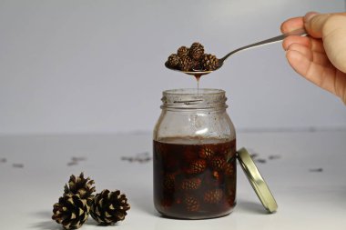 Sedir kozalakları, yararlı kış hazırlıkları dan reçel. vegan gıda, ham, sağlıklı gıda. olağandışı tatlılar. sıvı akışı aşağı akan kaşık içinde diken diken. Beyaz arka plan. elinde kaşık alın