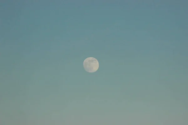 La luna contra el cielo azul y al lado del avión vuela. Estaba oscureciendo, el atardecer y la salida de la luna. día y noche cambio — Foto de Stock