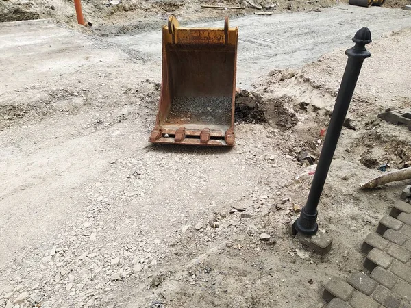 掘削機からのバケツはアスファルトなしで道路上にあります。道路の修理、アスファルト、レール、舗装スラブやフェンスの交換。パイプラインと排水システムの溝を掘る. — ストック写真