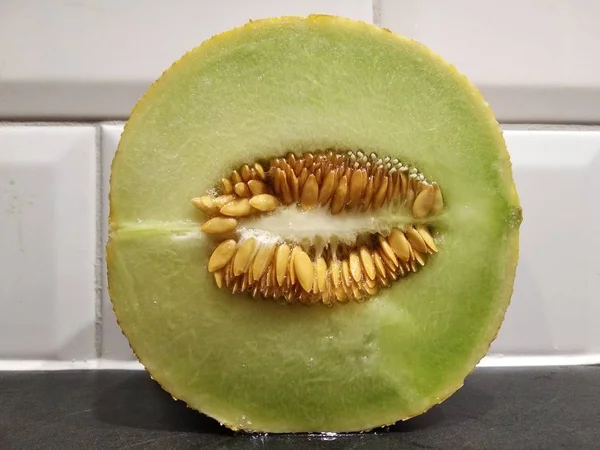 Um pedaço de melão com sementes está sobre a mesa, cortar melão verde branco. contra a parede de tijolo branco — Fotografia de Stock