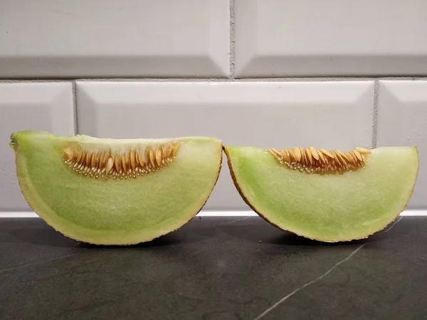 Um pedaço de melão com sementes está sobre a mesa, cortar melão verde branco. contra a parede de tijolo branco — Fotografia de Stock