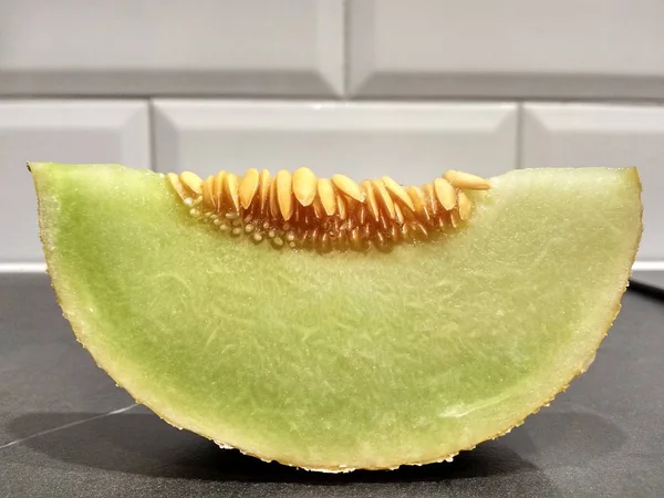 Um pedaço de melão com sementes está sobre a mesa, cortar melão verde branco. contra a parede de tijolo branco — Fotografia de Stock