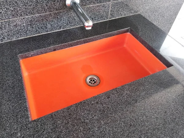 Orangefarbene tiefe und breite Spüle auf einer steinernen Arbeitsplatte mit Wasserhahn und Wasserablauf. modernes Design. — Stockfoto