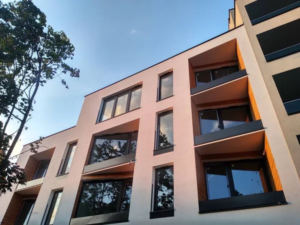 Современный многоэтажный жилой комплекс в городе. Окна и лоджии дома на закате среди деревьев. тенденции в строительстве, отделка балконов с деревом, фасад дома — стоковое фото