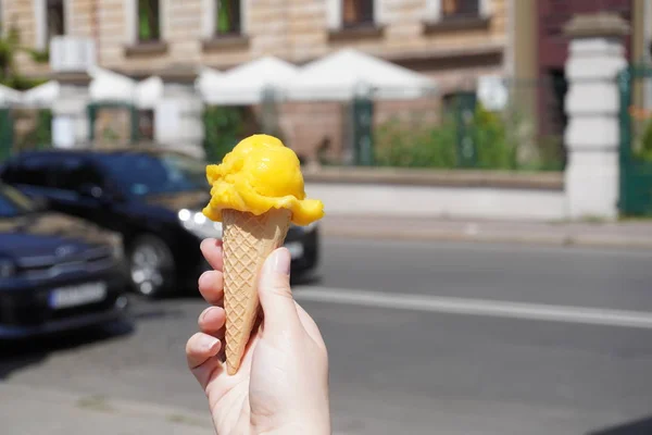 yellow hand made ice cream in a waffle cone girl holding in her hand against the blur of the old town on a Sunny hot day. cold dessert on a warm day. laconic for children and adults